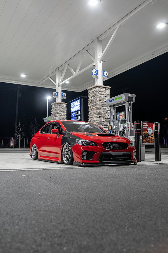gallery-02 A modern red sports car at a gas station under bright lights at night, conveying a theme of automotive technology.